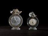 two glass figurines with a clock in the middle of them
