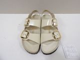 white sandals with gold buckles on them sitting on a white surface