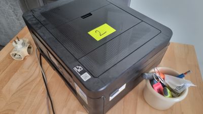 une imprimante posée sur un bureau, sur laquelle est collé un autocollant jaune