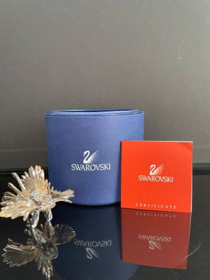 une petite fleur en argent posée sur une table, à côté d'une boîte de Swarovski