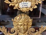 a gold clock with a face on it in a glass case
