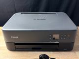 a canon printer sitting on top of a wooden table next to a charger