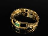 a close up of a gold bracelet with a green stone on it