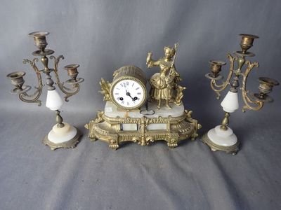 une horloge posée sur une table, à côté de trois chandeliers