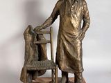 statue en bronze représentant un homme debout à côté d'une chaise, en compagnie d'un chien