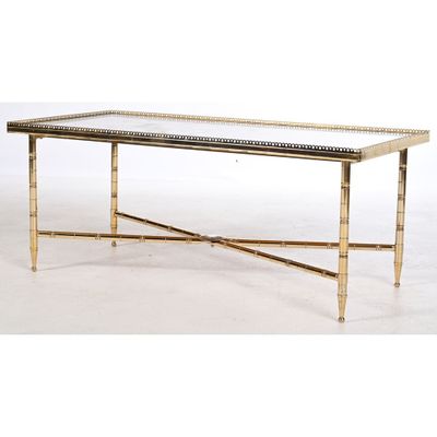 une table basse en laiton avec un plateau en verre et des pieds en métal