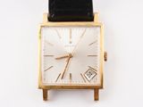 une montre en or avec un bracelet en cuir noir posée sur un fond blanc