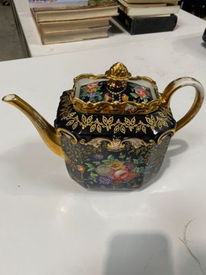 une théière noire et dorée posée sur une table blanche