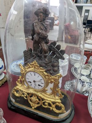 une horloge posée sur une table, sous un dôme en verre