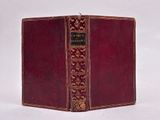 an old book with a red cover sitting on top of a white surface