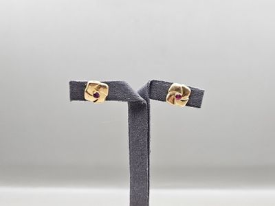 une paire de boucles d'oreilles en or et rubis posée sur un socle noir