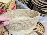 a person holding a straw hat in front of a pile of straw hats