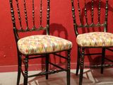 pair of antique chairs with upholstered seats in front of a red wall