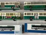 six green and white buses are lined up on a white surface