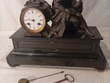 une statue représentant un homme assis sur une table, à côté d'une horloge