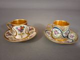 two cups and saucers with floral designs on them on a table
