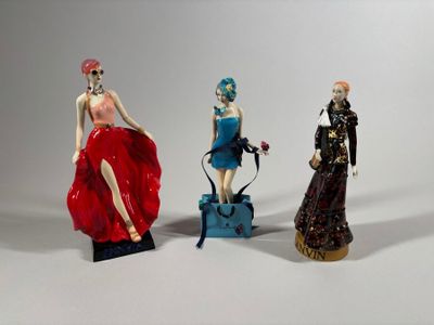 trois figurines représentant des femmes vêtues de styles et de couleurs variés