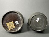 pair of old metal pots with labels on them sitting on a table