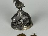 un petit oiseau en métal posé sur un rocher, à côté de deux pièces de monnaie