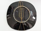 a black plate with a gold wire hanging on the wall