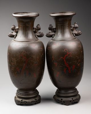 pair of antique chinese bronze vases on pedestals against a gray background