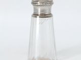une salière en verre avec un couvercle argenté, posée sur une surface blanche