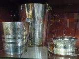une étagère en verre sur laquelle sont posées des tasses en argent, dont une