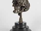 bronze skull head on a black marble base with a white background
