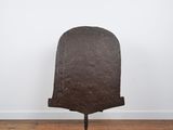 un vieux casque en fer posé sur un socle métallique, sur un plancher en bois