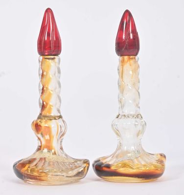 two glass candlesticks with red tops on a white background