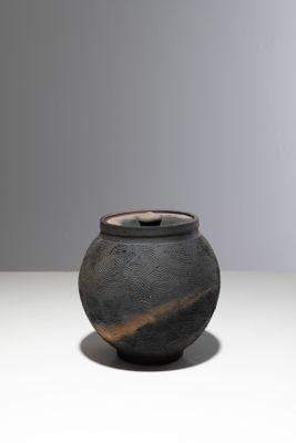 un vase noir posé sur une table, sur fond blanc