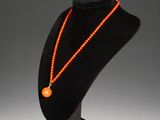 an orange beaded necklace on a black mannequin