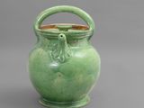 un vase vert muni d'une anse et d'une poignée, sur fond gris