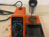 an orange soldering machine sitting on top of a table next to a cup