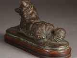 statue of a dog laying on a wooden base on a gray surface