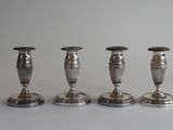 trois bougeoirs en argent sont alignés sur une surface blanche