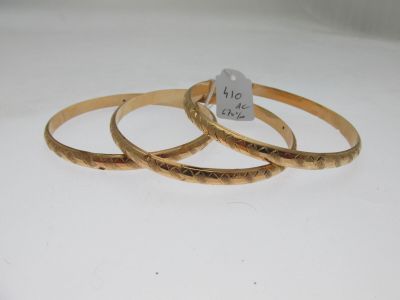 trois bracelets rigides en or posés sur une surface blanche, avec une étiquette de prix
