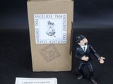 une petite figurine représentant un homme en smoking, à côté d'une boîte
