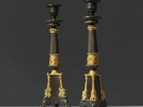 Deux bougies noires et dorées sont posées sur une table blanche.