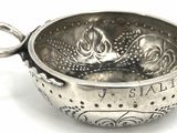 a silver bowl with a handle on a white surface