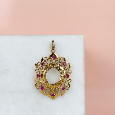 a close up of a gold pendant with pink stones on a marble surface