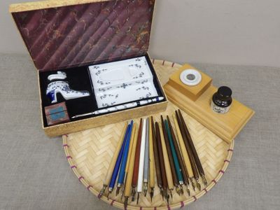 a wooden box with pens, a pen holder, and other items on a table