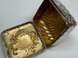 a small silver box with a gold design on it