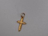 un petit pendentif en forme de croix en or sur un fond gris