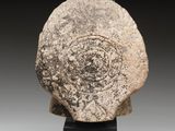 an ancient stone head with a circular design on it