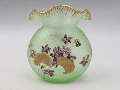un vase vert contenant des fleurs violettes, posé sur une surface blanche