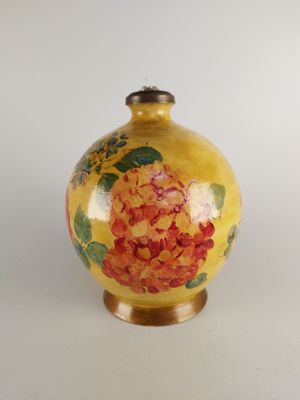 un vase jaune orné de fleurs rouges, posé sur un fond blanc