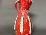a red and white vase sitting on a gray surface