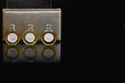 three bottles of perfume sitting on a table next to a suitcase