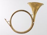 an antique brass french horn on a stand against a white background